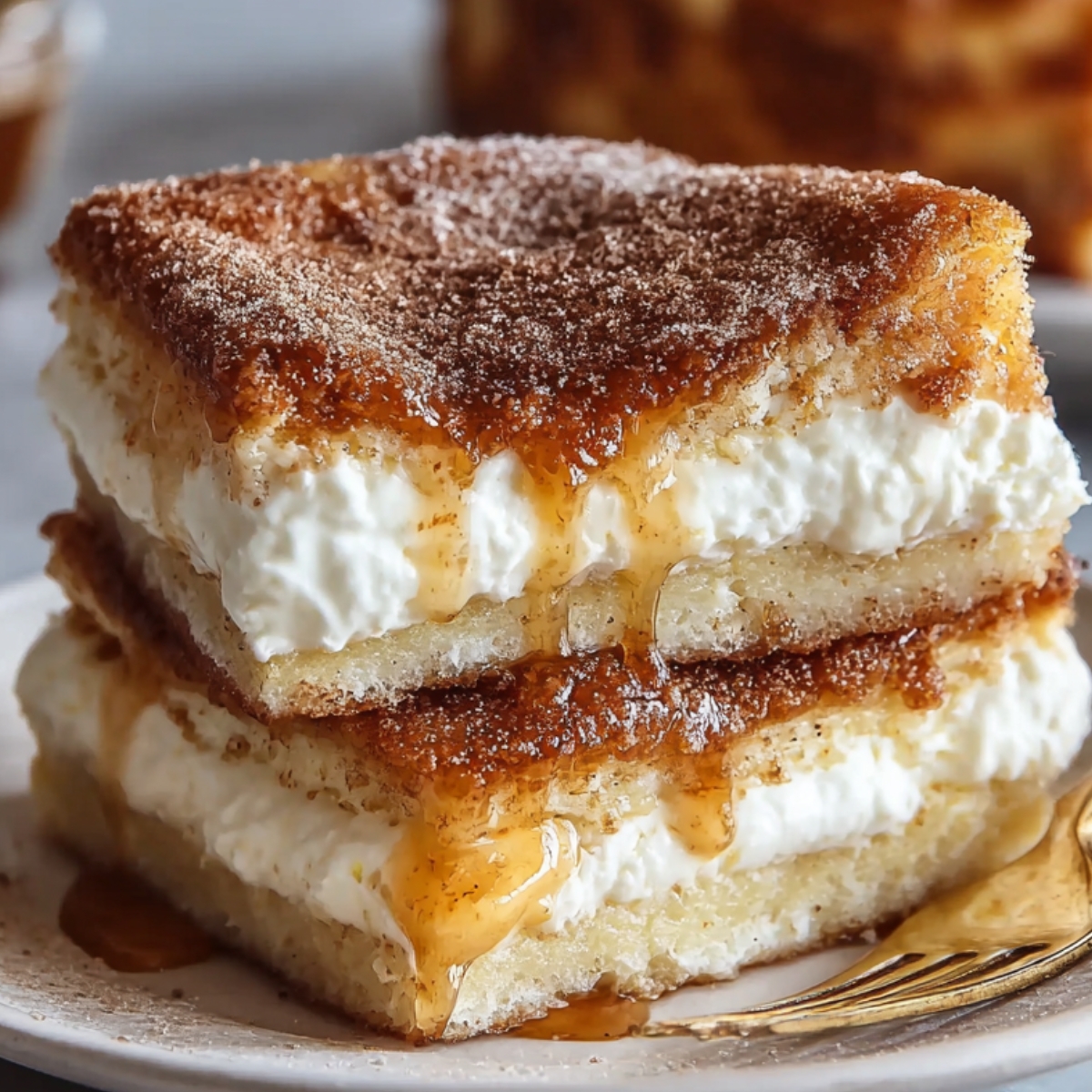 "A square slice of Sopapilla Cheesecake topped with cinnamon sugar and drizzled with honey, layered with creamy filling."