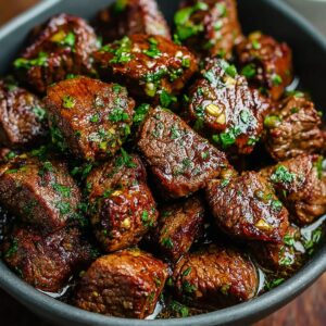 - Dark bowl filled with seared garlic butter steak bites coated in herbs and garlic.