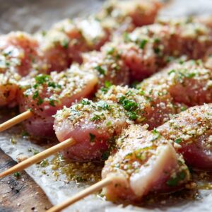 Raw chicken skewers coated with parmesan, garlic, herbs, and seasoning on parchment.