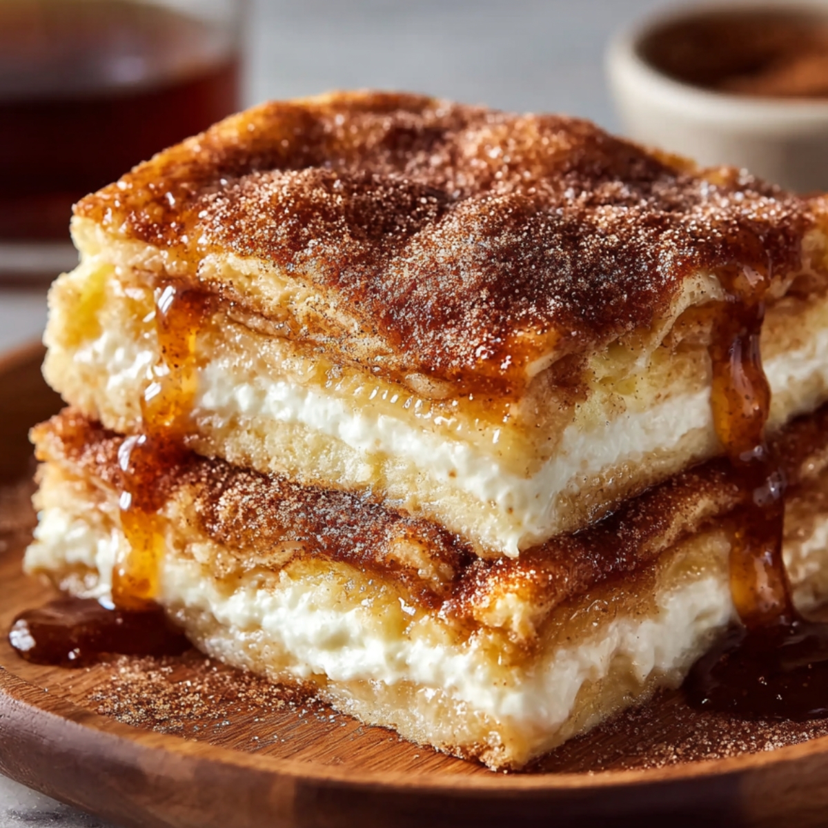 "Two stacked slices of Sopapilla Cheesecake on a wooden plate, layered with cream cheese filling and drizzled with honey and cinnamon sugar."