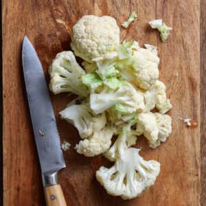 Chopped cauliflower florets on a cutting board with a knife