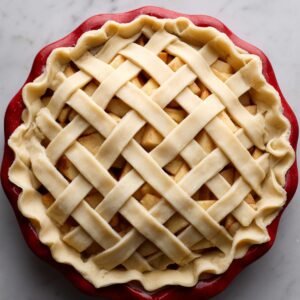Unbaked apple pie in a red pie dish with a lattice crust pattern on top of the apple filling.