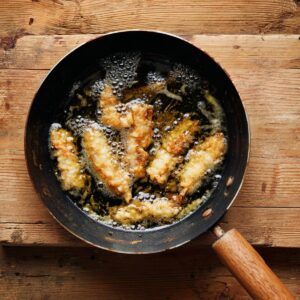 Fish fillets frying in a skillet until golden brown.