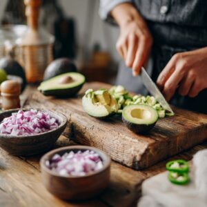 Person chopping avocado on a cutting board with onions and jalapeños nearby.