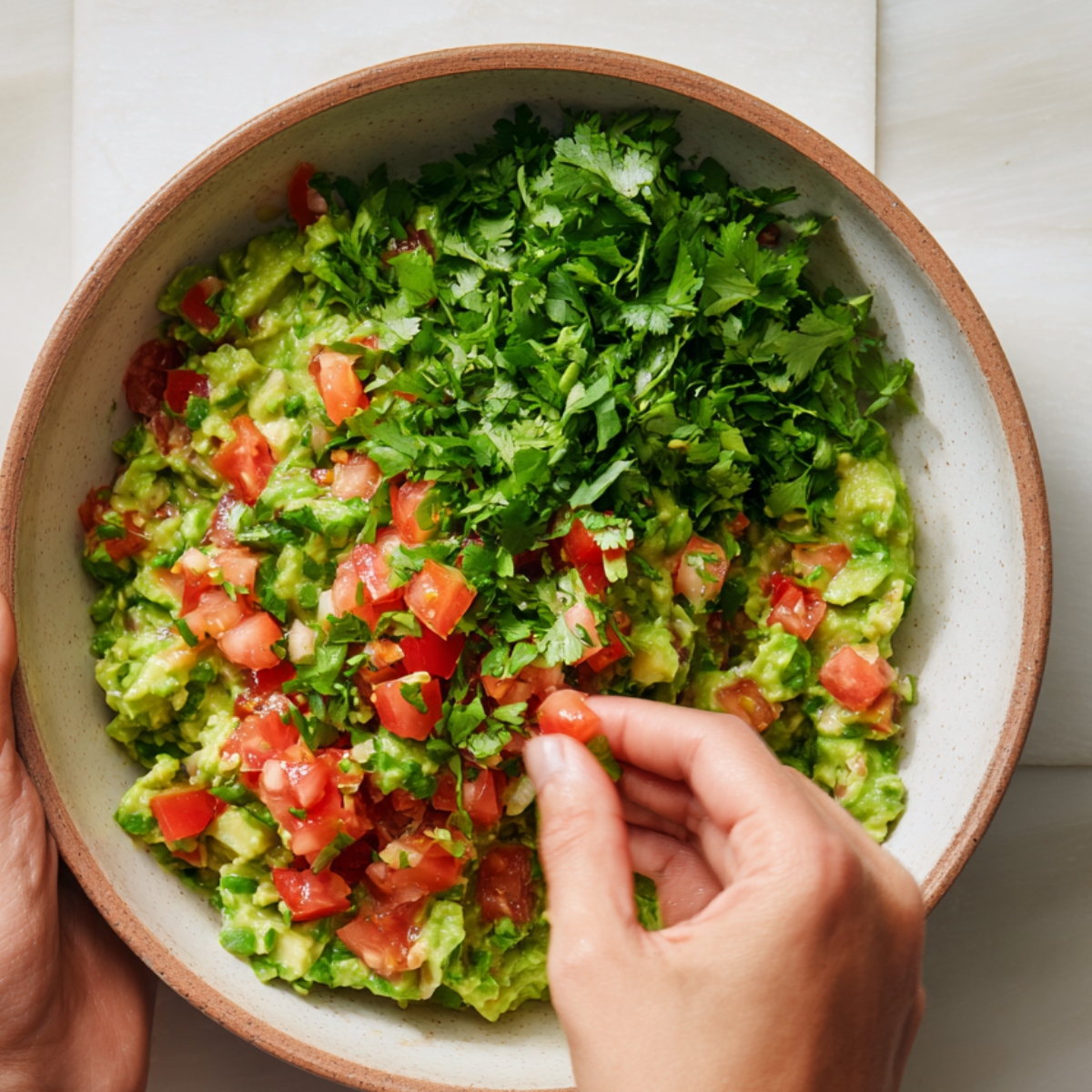 Bowl of guacamole topped with chopped tomatoes and fresh cilantro