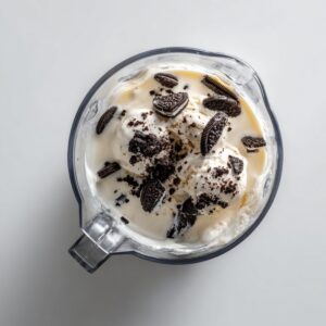 A blender filled with scoops of vanilla ice cream, milk, and crushed Oreo cookies, ready to be blended into a milkshake