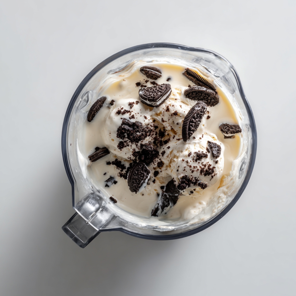 A blender filled with scoops of vanilla ice cream, milk, and crushed Oreo cookies, ready to be blended into a milkshake