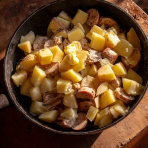Hands mixing diced potatoes and sausage with ranch seasoning and oil in a large bowl before baking.