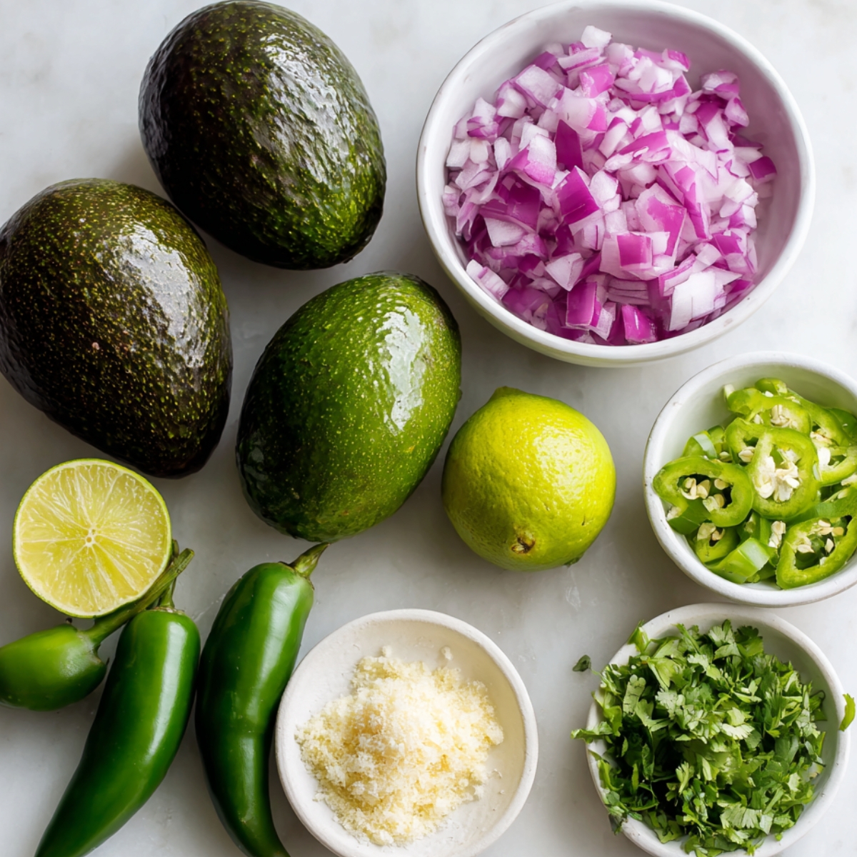 Fresh avocados, lime, jalapeños, red onion, cilantro, and cheese on a table