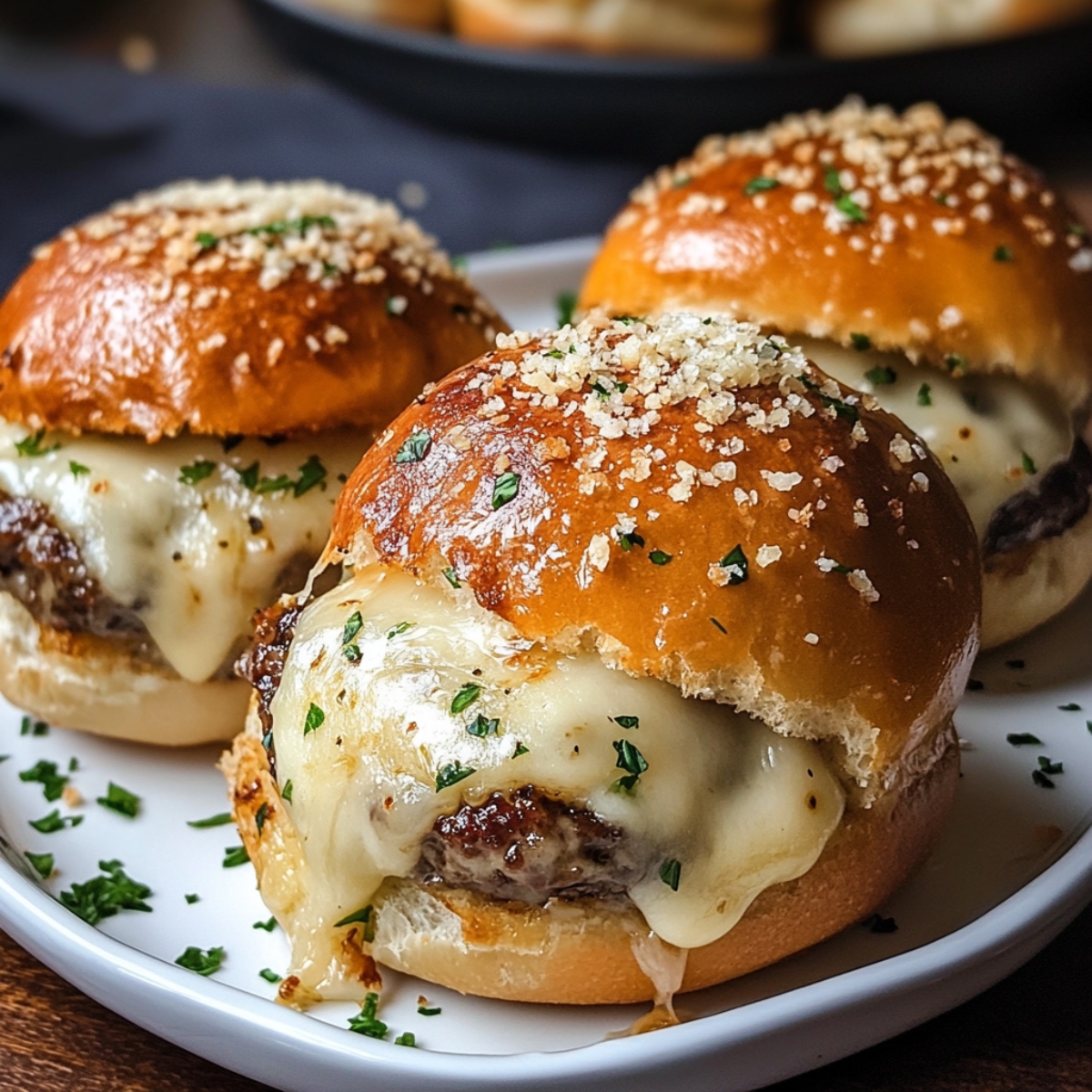 Garlic parmesan cheeseburger Bombs sliders on a plate, each with melted cheese oozing out, topped with parsley and parmesan flakes.