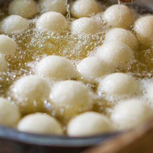 A close-up shot of white dough balls deep frying in hot oil, creating bubbles around them.