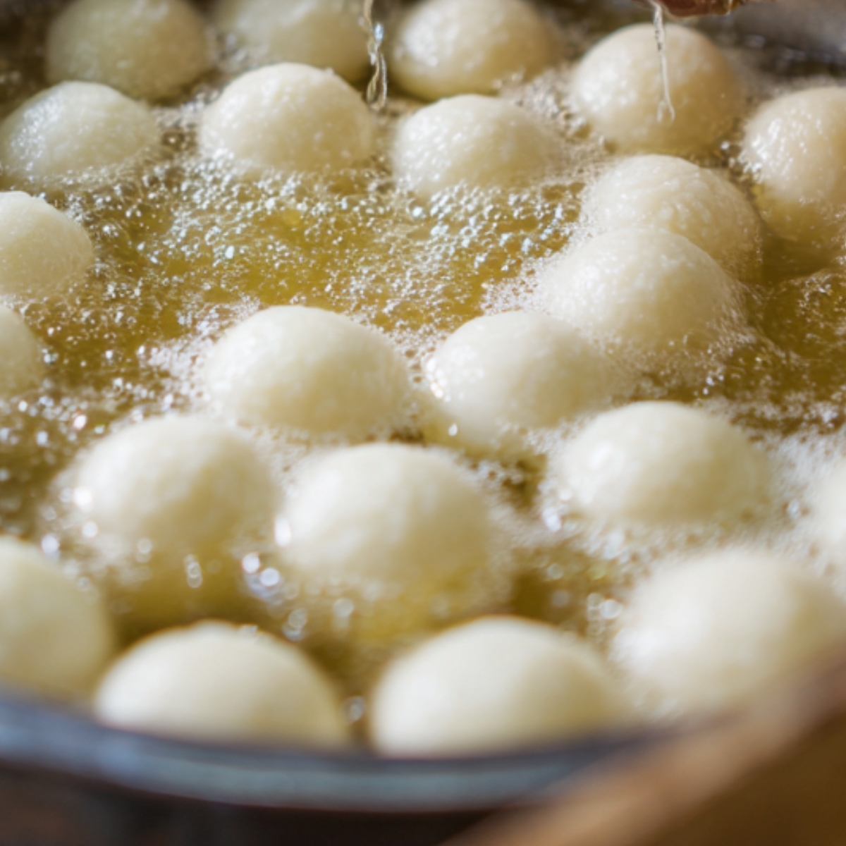 A close-up shot of white dough balls deep frying in hot oil, creating bubbles around them.