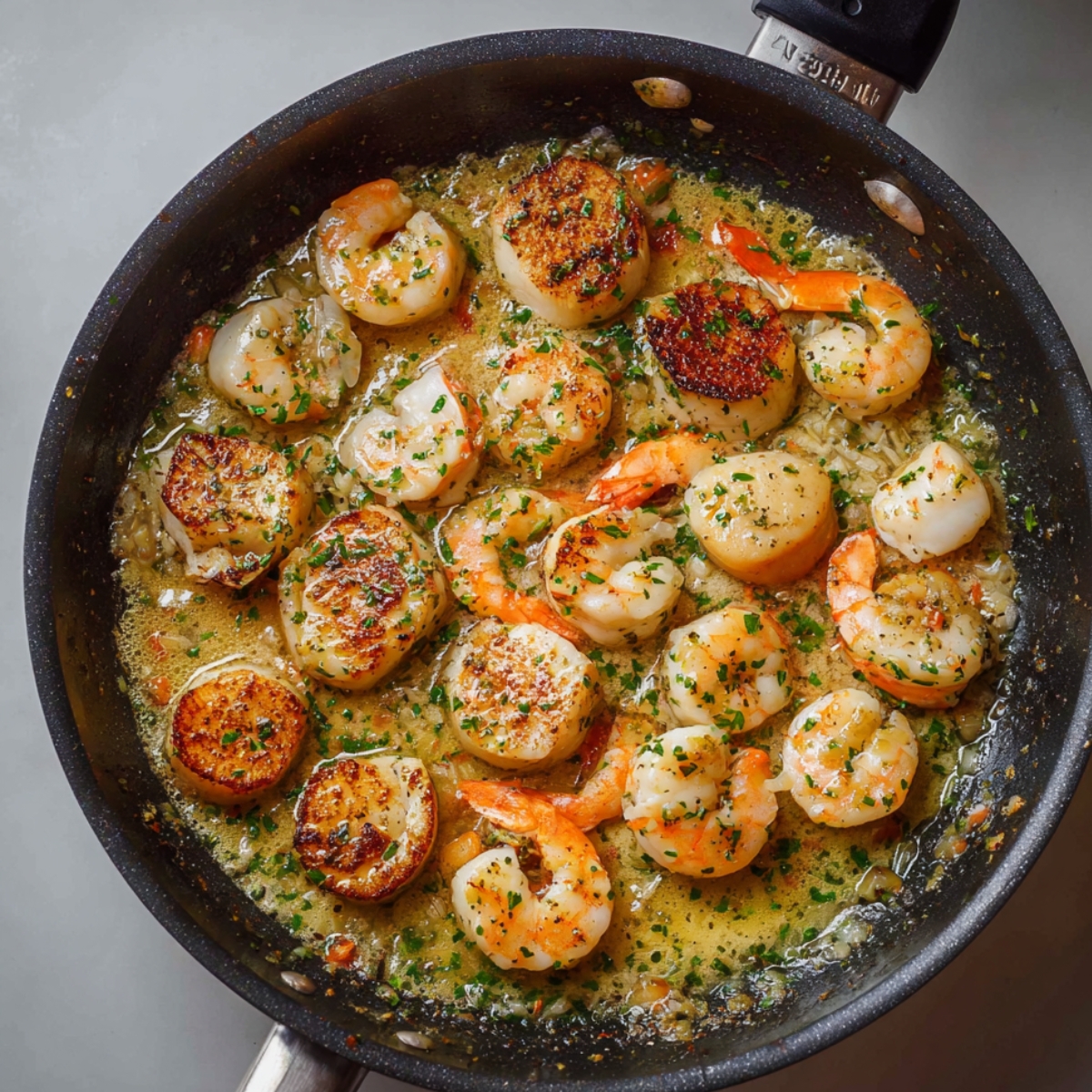 Sautéed shrimp and scallops in a skillet with garlic butter sauce and chopped parsley, seared to a golden brown.