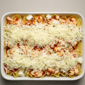 Unbaked seafood lasagna in a white casserole dish, layered with shrimp, ricotta cheese, red sauce, and topped generously with shredded mozzarella cheese.