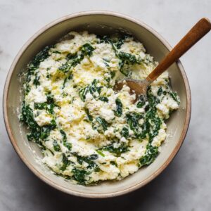A bowl filled with ricotta cheese and spinach, stirred together to make the filling for stuffed manicotti.
