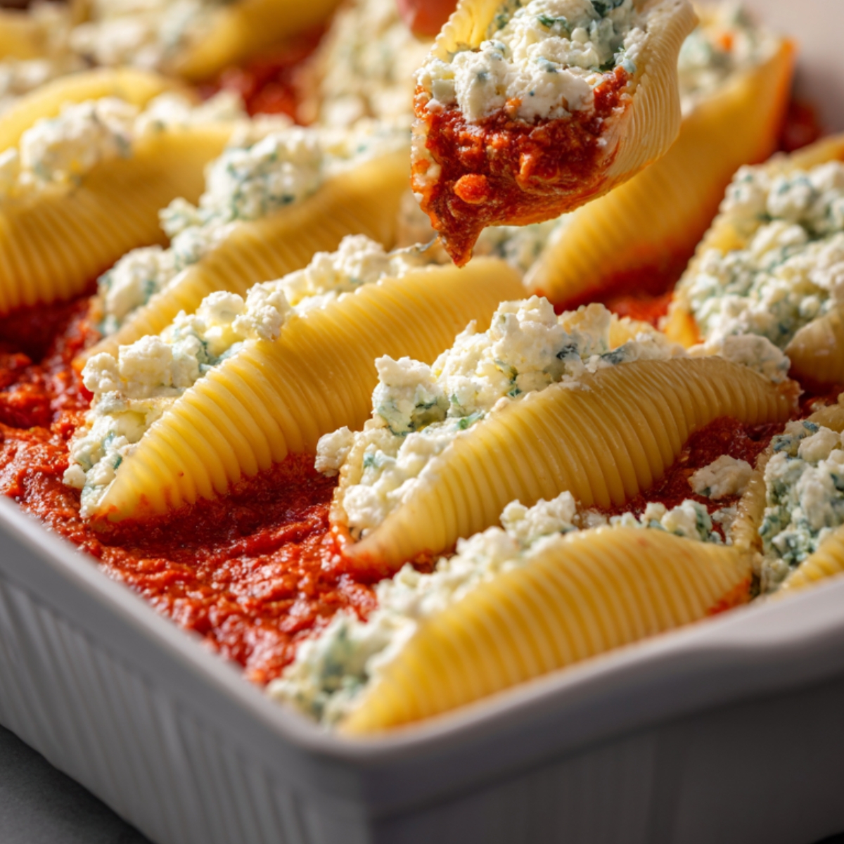 A close-up shot of stuffed manicotti shells filled with a ricotta mixture and placed in tomato sauce, with one shell being lifted with a spoon.