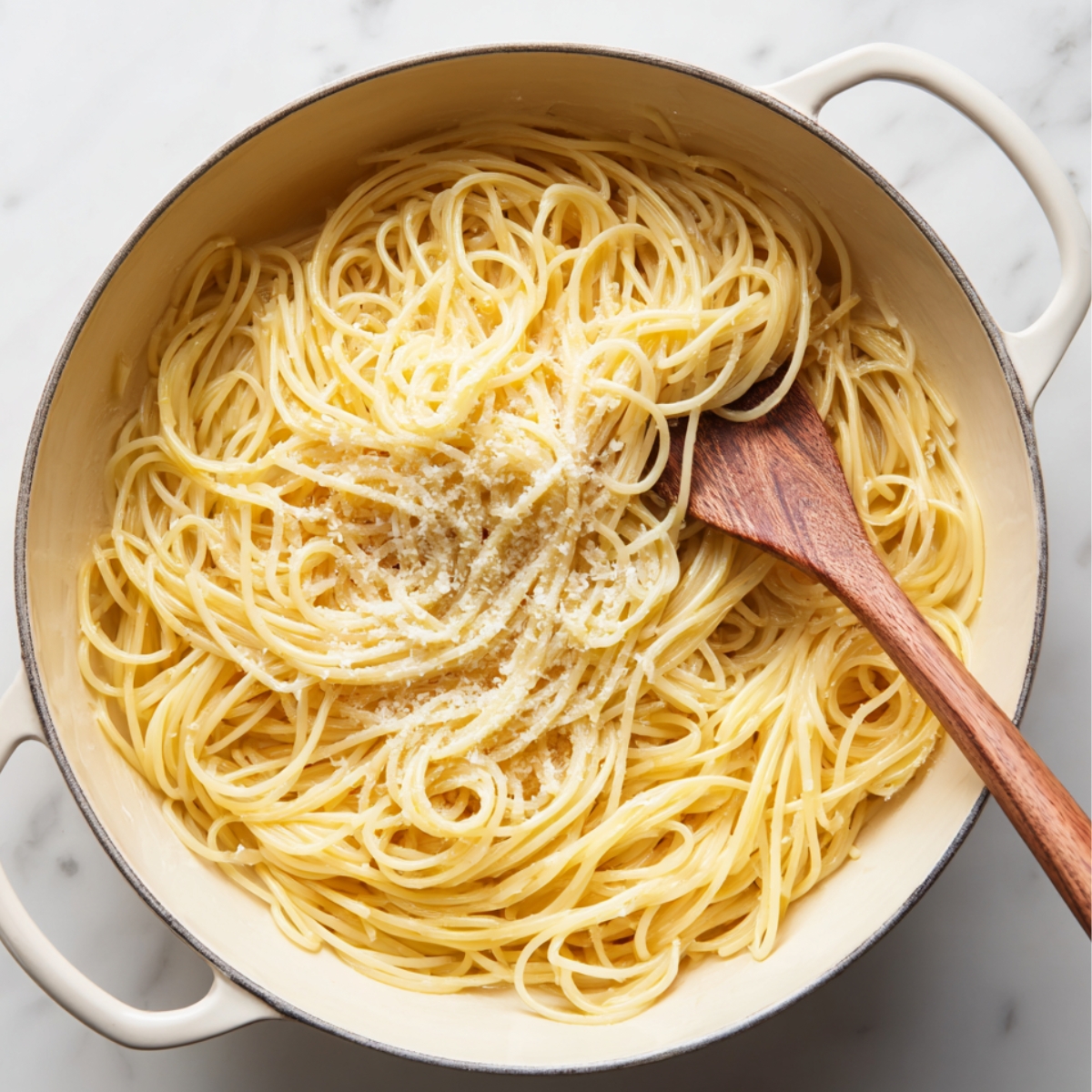 Cooked spaghetti pasta in a large pot, tossed with grated parmesan cheese and a wooden spoon.
