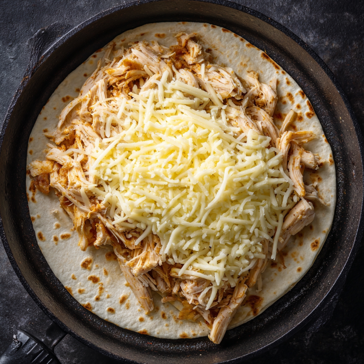 "Open quesadilla in a skillet filled with shredded chicken and grated cheese before folding and cooking."