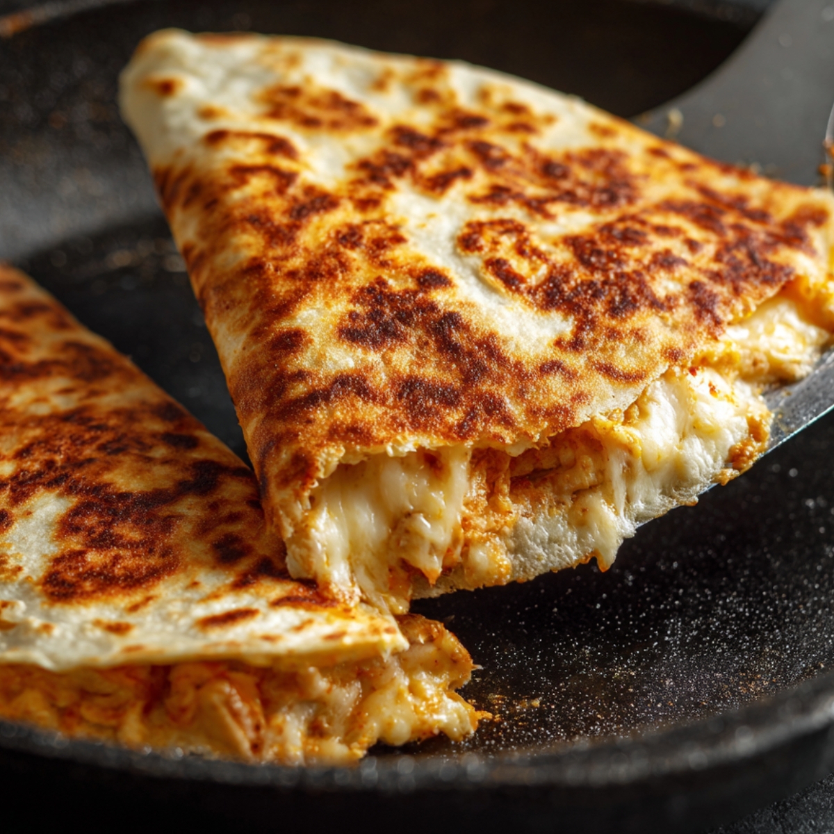 "Close-up of a cheesy chicken quesadilla being lifted from a skillet, showing golden-brown crust and melted cheese."