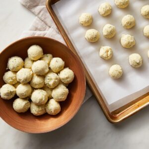 Bowl of scooped key lime truffle mixture shaped into small balls, with more lined neatly on a parchment-lined baking sheet.