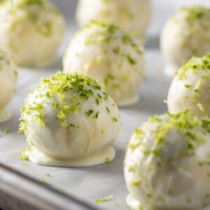 Close-up of white chocolate-coated key lime truffles sprinkled with fresh lime zest, set on a parchment-lined baking sheet.