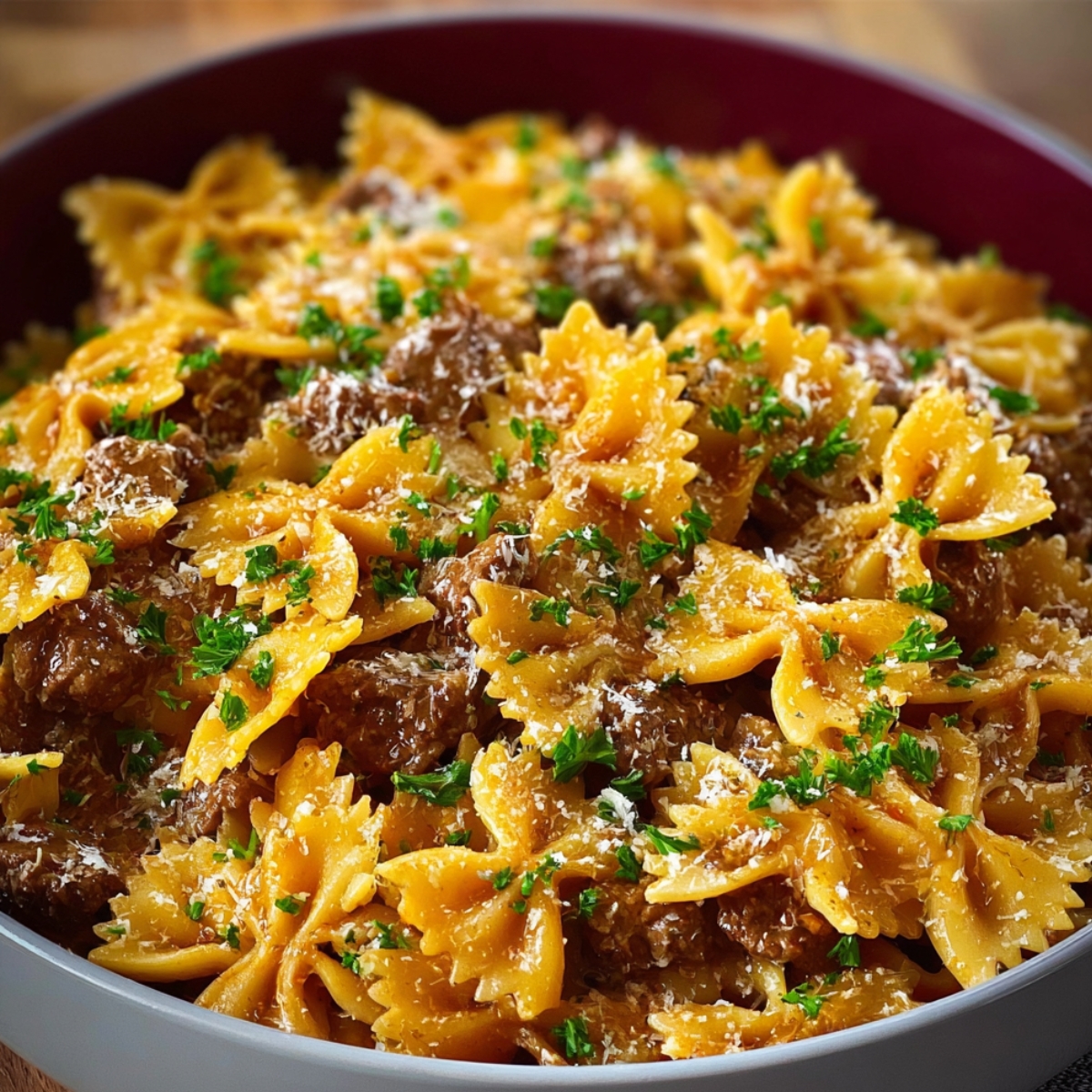 A finished dish of beef and bowtie pasta mixed with beef and sauce, garnished with chopped parsley and grated cheese.