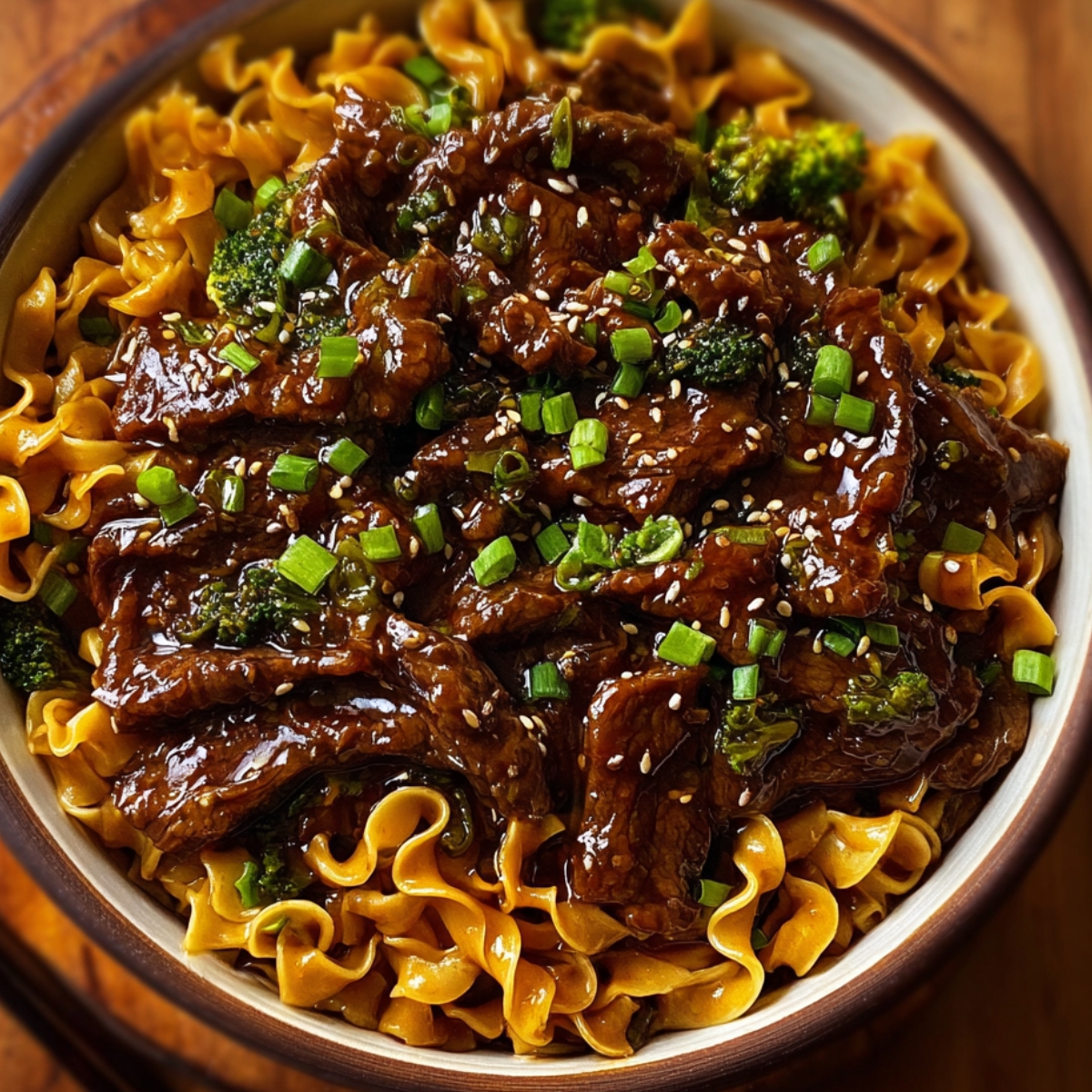 “Bowl of homemade beef and noodles topped with tender beef slices, sesame seeds, and green onions over egg noodles.”