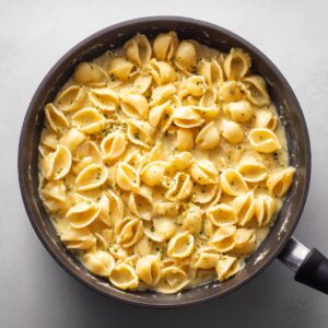 A pan of cooked shell pasta coated in a creamy cheese sauce, sprinkled with herbs.