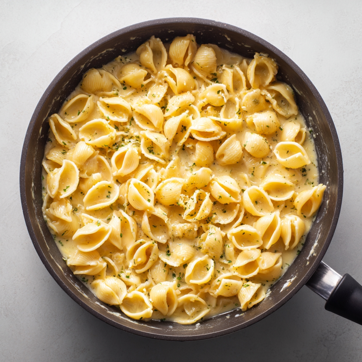 A pan of cooked shell pasta coated in a creamy cheese sauce, sprinkled with herbs.