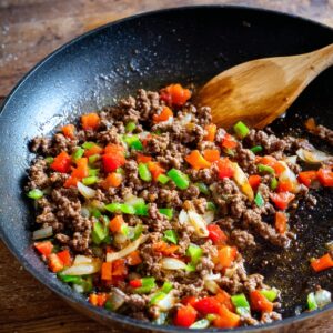 Ground beef cooked with diced red and green bell peppers and onions in a frying pan.