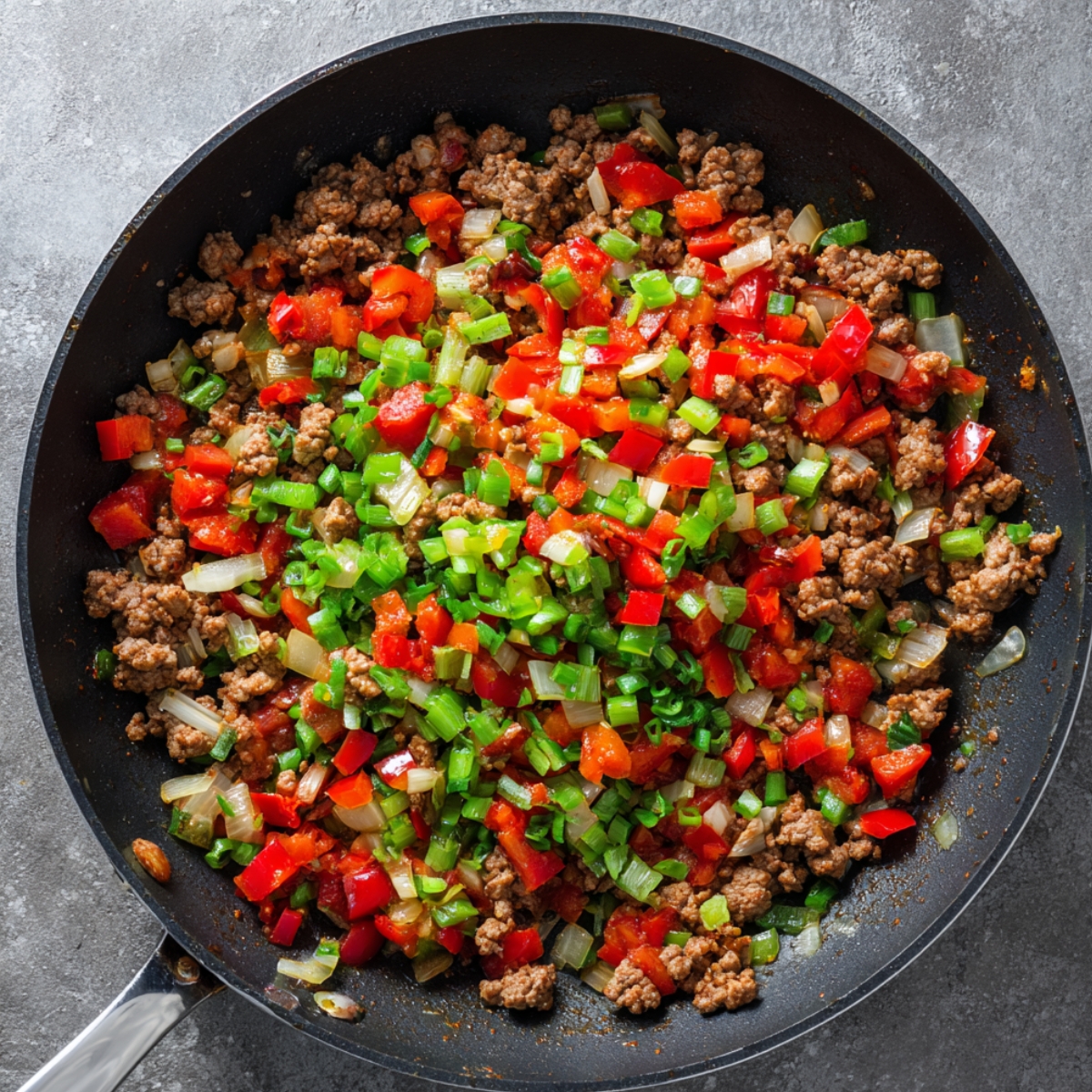 A skillet filled with ground beef, chopped red peppers, onions, and green onions, cooking together.