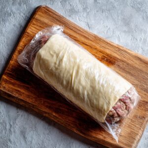 A Beef Wellington wrapped in puff pastry, still unbaked, placed on a wooden surface.