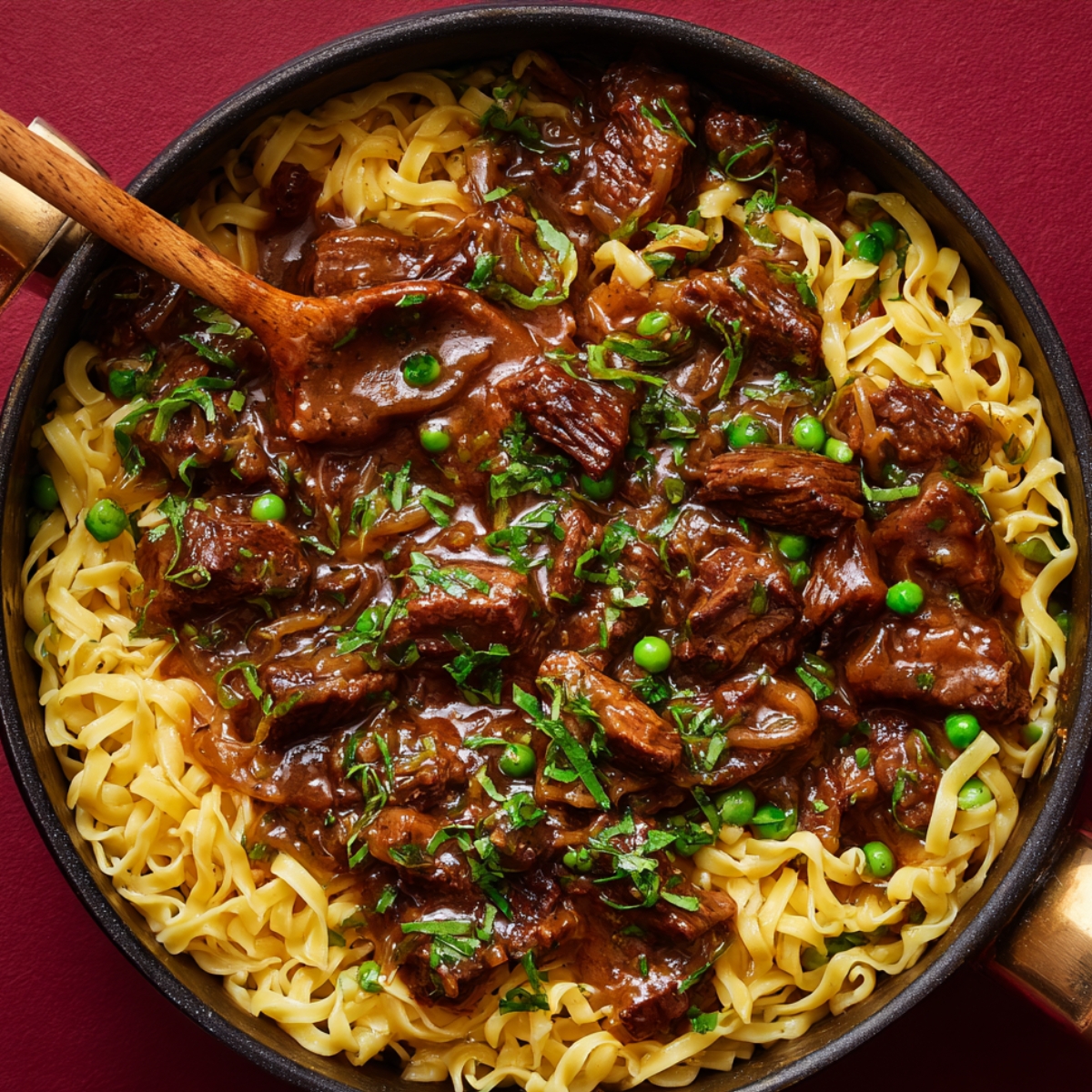 “Pan of beef and noodles in rich brown gravy, garnished with parsley and green peas, with a wooden spoon for serving.”