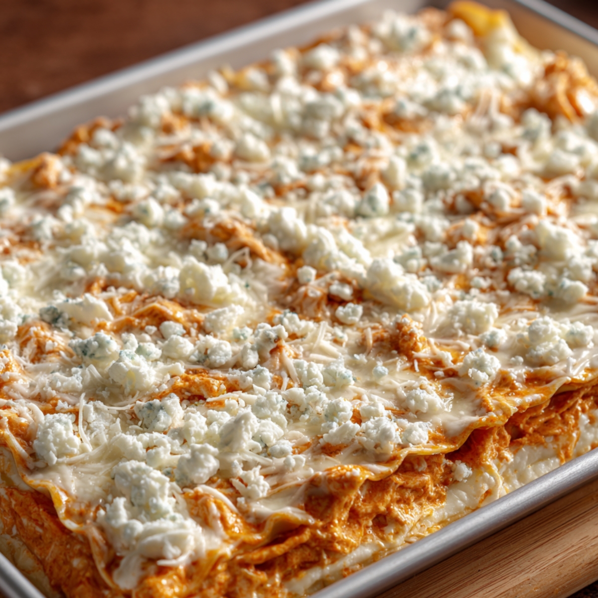 A baking dish of lasagna layered with creamy buffalo sauce and cheese, topped with crumbled blue cheese.