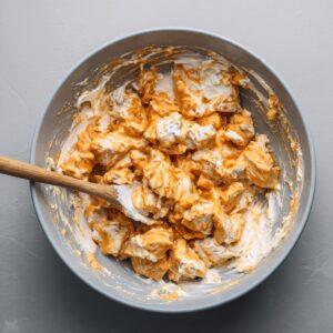 A bowl of buffalo chicken mixture combined with creamy sauce being stirred with a spatula.