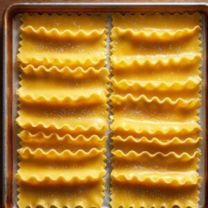 A baking sheet lined with parchment paper holding neatly arranged uncooked lasagna noodles, lightly dusted with flour and ready for cooking.
