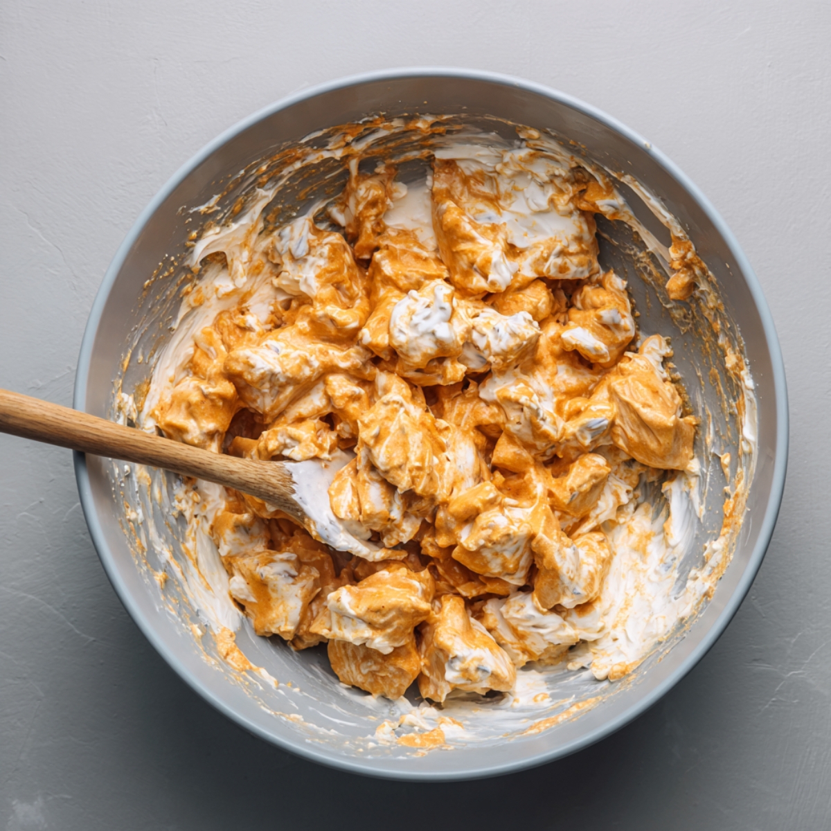 A bowl of buffalo chicken mixture combined with creamy sauce being stirred with a spatula.