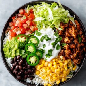 A colorful burrito bowl with rice, black beans, corn, shredded lettuce, seasoned meat, guacamole, sliced jalapeños, diced tomatoes, sour cream, and cilantro arranged neatly in sections.