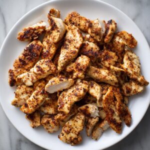 A plate filled with small pieces of grilled chicken, lightly charred and arranged on a white plate.