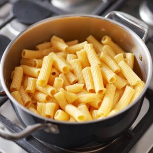 A close-up of rigatoni pasta being boiled in a silver pot on a stove.