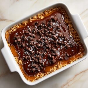 Baking dish with a caramel and chocolate layer topped with chocolate chips and coarse sea salt over a crumb crust.