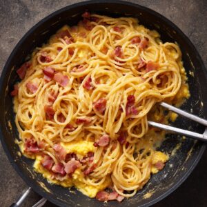 A pan with cooked spaghetti carbonara, featuring crispy bacon and creamy egg mixture.