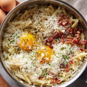 A pan of spaghetti carbonara with raw egg yolks, bacon, grated cheese, and freshly cracked black pepper.