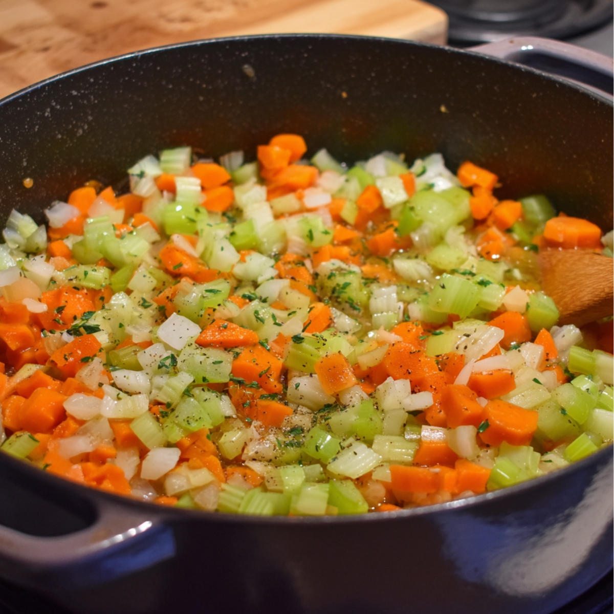 “Chopped carrots, celery, and onions sautéing in a large pot with herbs and seasoning, forming the base for chicken noodle soup or pasta.”