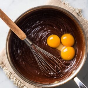 A saucepan containing melted chocolate and butter mixture with three egg yolks added, ready to be whisked in.