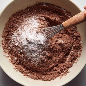 A bowl of dry brownie ingredients including cocoa powder, flour, and sugar being whisked together.