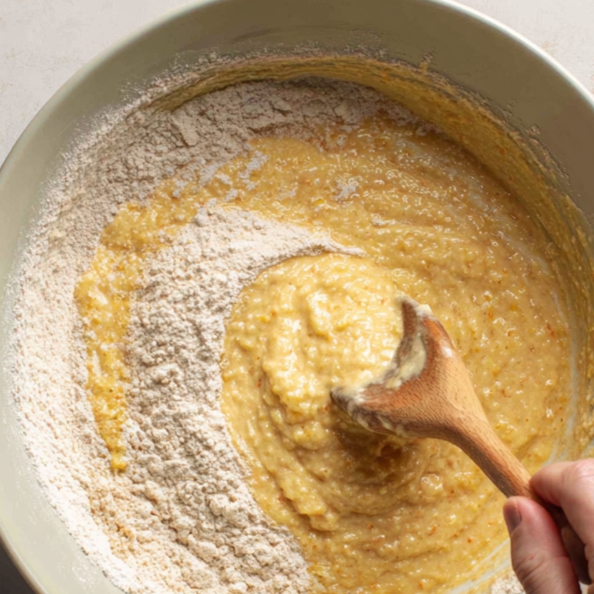 Mixing cornbread batter in a bowl with a wooden spoon, combining wet and dry ingredients.