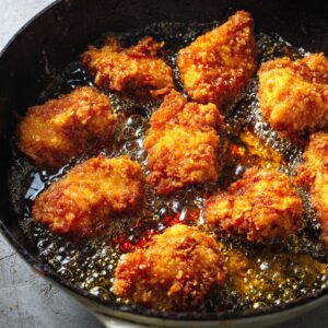 Chicken pieces frying in hot oil, crispy and golden brown.