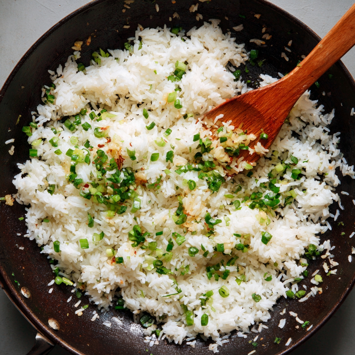 A close-up of a pan with fluffy white rice being stirred with green onions, giving the dish a simple and fresh look.