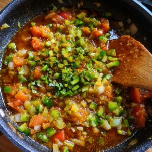A pan with chopped tomatoes, onions, green chilies, and spices, cooking together in a mix of oil.